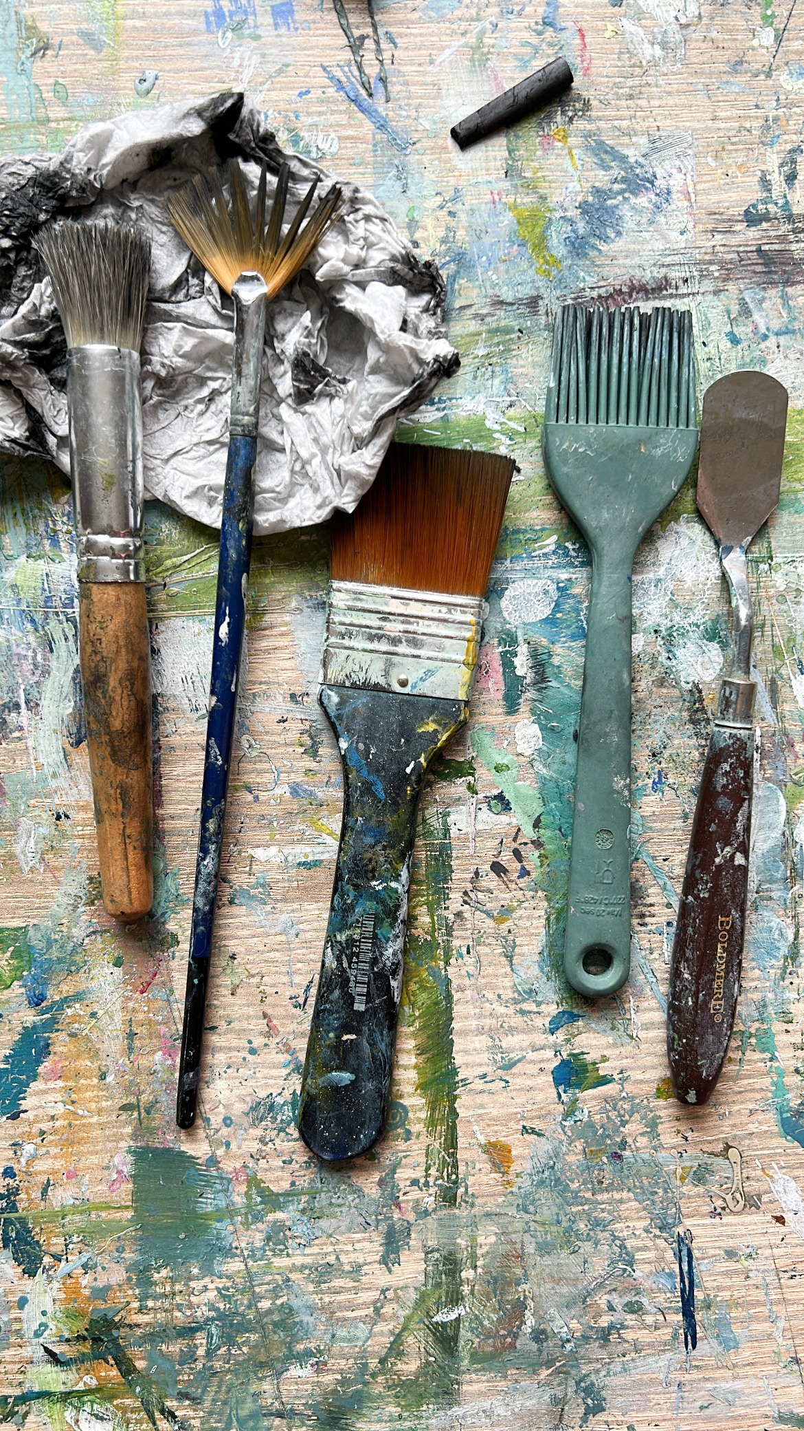 paintbrushes and art making tools on a table covered in paint